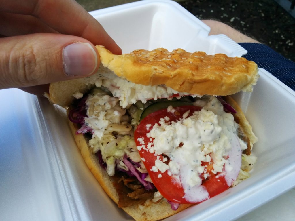 A photo of a döner kebab which is crisp bread with grilled lamb meat, lettuce, tomatoes, red cabbage, feta cheese, and tzatziki sauce in it.